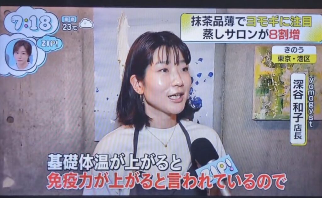 Woman being interviewed on a Japanese TV program, speaking into a microphone with on-screen Japanese captions at the bottom and a small guest image in the upper-left corner.